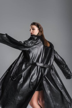 young fashionable woman posing in black leather coat isolated on grey