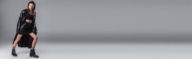full length of young woman in stylish leather clothing standing on grey background, banner