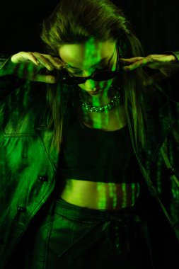 young woman in crop top and leather coat posing with bowed head isolated on black