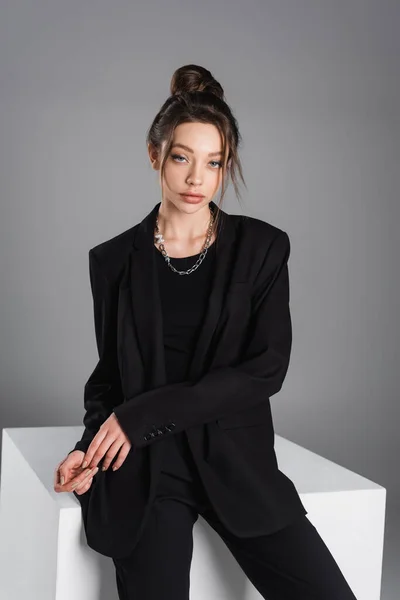 Trendy Woman Black Jacket Sitting White Cube Looking Camera Isolated — Foto de Stock