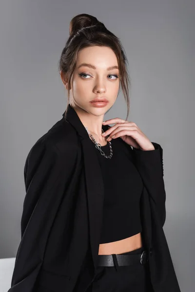 pretty woman in black jacket and silver necklace looking away isolated on grey