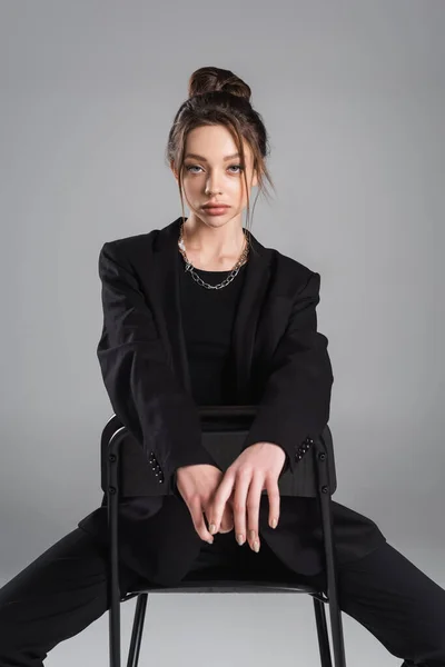 Brunette Woman Black Clothes Sitting Chair Looking Camera Isolated Grey — Zdjęcie stockowe