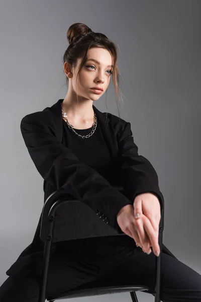 Fashionable Woman Black Blazer Sitting Chair Looking Away Isolated Grey — стоковое фото