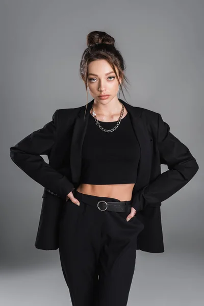 pretty woman in crop top and black suit standing with hands on hips isolated on grey
