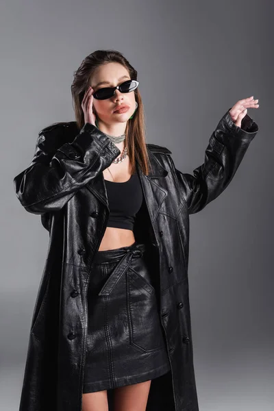 Young Brunette Woman Black Leather Coat Touching Stylish Sunglasses Isolated — стоковое фото