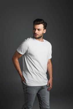 Young man in white t-shirt and jeans looking away isolated on grey 