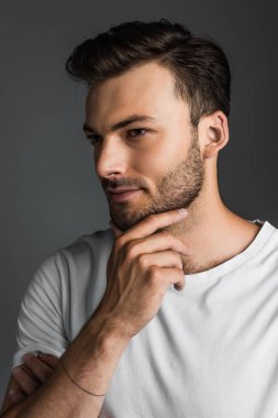 Young bearded man touching chin isolated on grey 