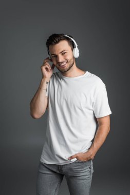 Smiling man in t-shirt and jeans using headphones isolated on grey 