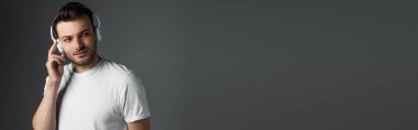 Brunette man listening music in headphones isolated on grey, banner 