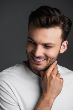 Happy man touching neck and looking away isolated on grey 