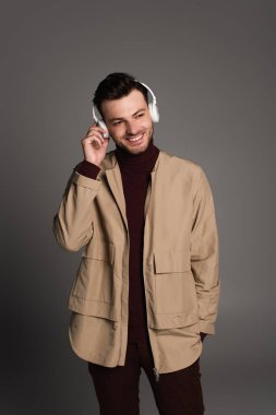 Smiling man in autumn outfit listening music in headphones isolated on grey 