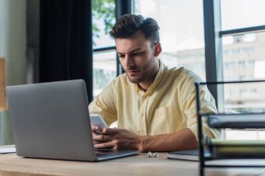 Businessman using smartphone near laptop and earphones on table in office 