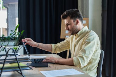 Side view of businessman using laptop near documents on table in office 