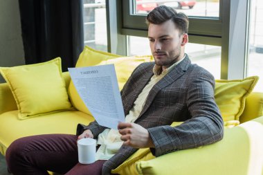 Businessman holding contract and cup on couch in office 