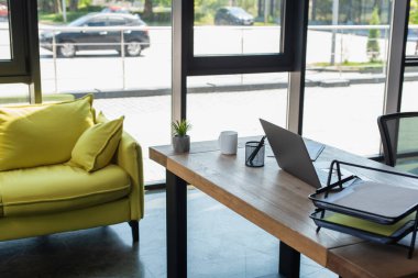 Papers and laptop on working table near couch in office 