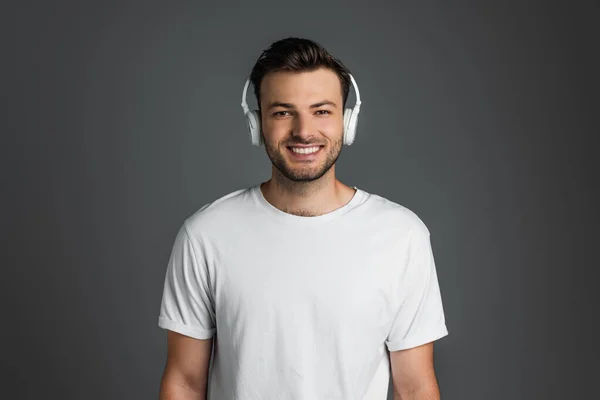 Happy man in white t-shirt and headphones looking at camera isolated on grey
