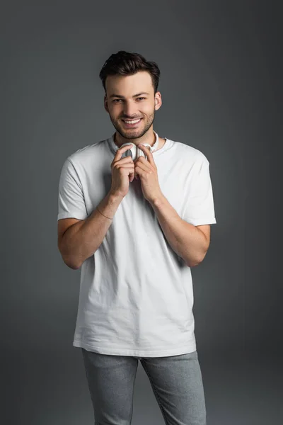 Positive Man Holding Headphones Looking Camera Isolated Grey — Stok fotoğraf