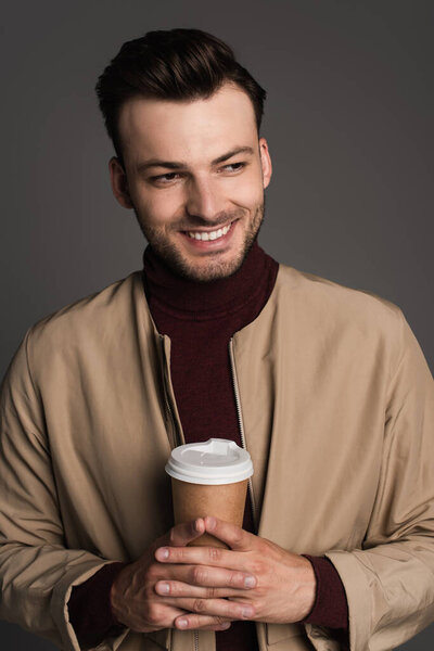 Portrait of positive man in autumn jacket holding takeaway drink isolated on grey 