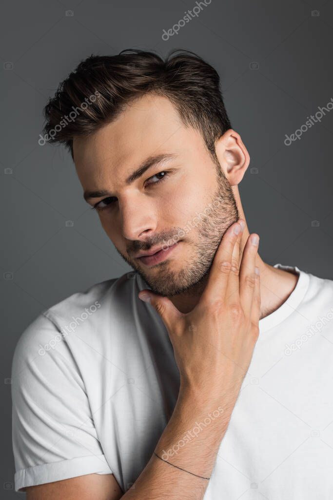 Portrait of brunette man touching beard and looking at camera isolated on grey 