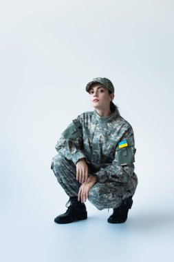 Soldier in uniform with ukrainian flag looking at camera on grey background
