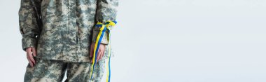 Cropped view of servicewoman in military uniform and blue and yellow ribbon on hand isolated on grey, banner  clipart