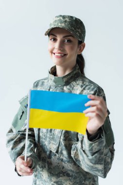 Portrait of smiling soldier holding blurred ukrainian flag isolated on grey 