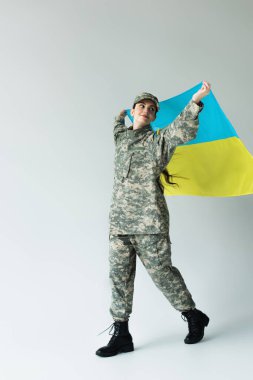 Gri arka planda yürürken elinde Ukrayna bayrağı tutan gülümseyen askerin tam uzunluğu