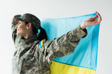 Gri üzerinde Ukrayna bayrağı taşıyan bulanık askerin yan görüntüsü 