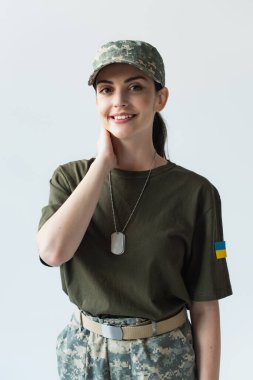 Positive soldier with ukrainian flag on uniform smiling at camera isolated on grey  clipart