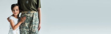 Child hugging mom in military uniform isolated on grey, banner 