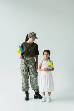 Soldier holding ukrainian flag near daughter on grey background