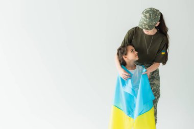 Soldier in camouflage uniform holding ukrainian flag near daughter isolated on grey 