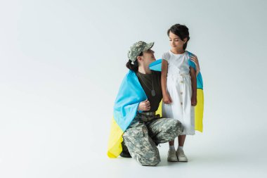 Positive soldier holding ukrainian flag near child on grey background