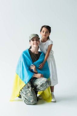 Kid hugging soldier in military uniform and ukrainian flag on grey background