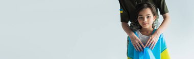 Servicewoman holding ukrainian flag near kid isolated on grey with copy space, banner 