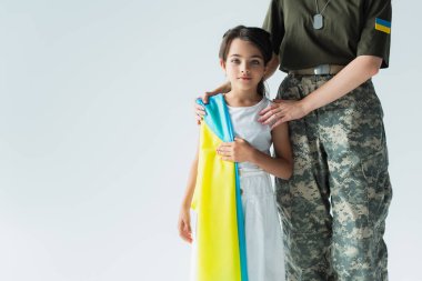 Soldier hugging child with ukrainian flag isolated on grey 