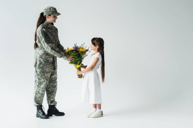Side view of child giving blue and yellow flowers to soldier on grey background