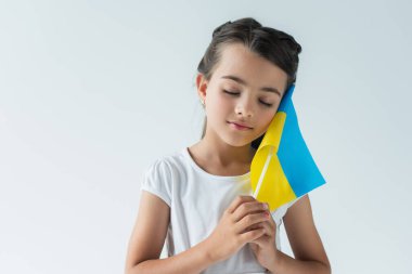 Kid with closed eyes holding ukrainian flag isolated on grey 