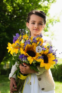 patriotic girl with blue and yellow bouquet looking at camera outdoors