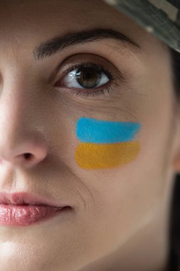 close up view of cropped woman with ukrainian flag painted on face