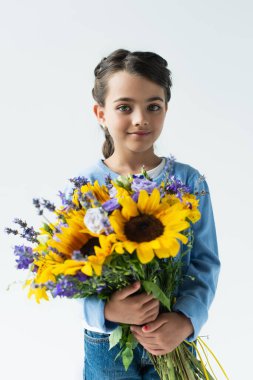 patriotic girl with blue and yellow bouquet smiling at camera isolated on grey