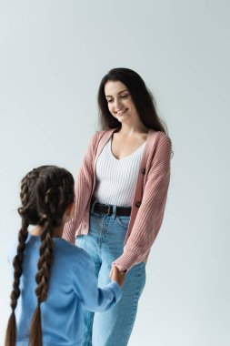 happy brunette woman holding hands of daughter isolated on grey