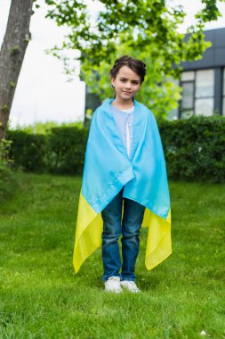 full length of girl with ukrainian flag looking at camera in city park clipart