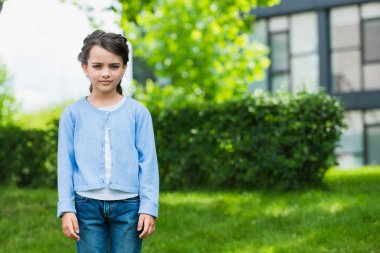 serious ukrainian child in blue jumper and jeans looking at camera on blurred background