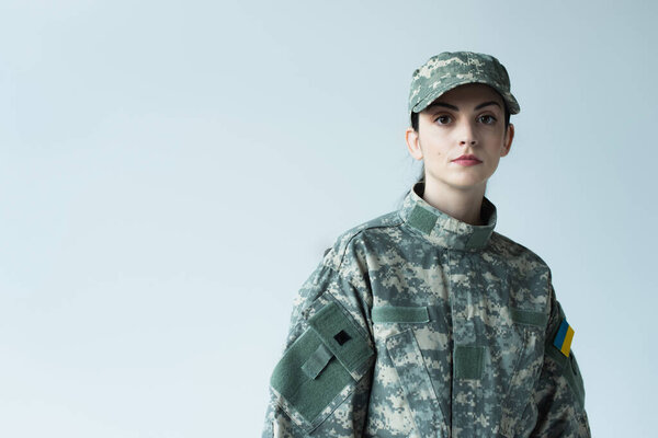 Soldier with ukrainian flag on military uniform looking at camera isolated on grey 