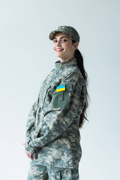 Positive soldier in cap and uniform with ukrainian flag isolated on grey 