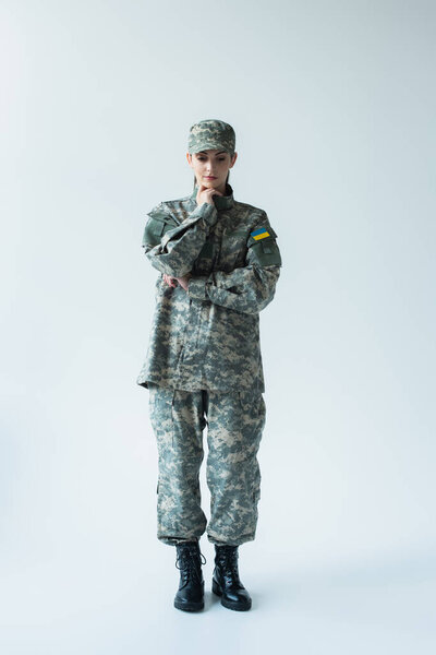 Full length of upset soldier in uniform with ukrainian flag on grey background