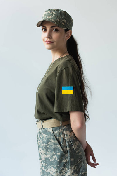 Young soldier with ukrainian flag on chevron looking at camera isolated on grey 