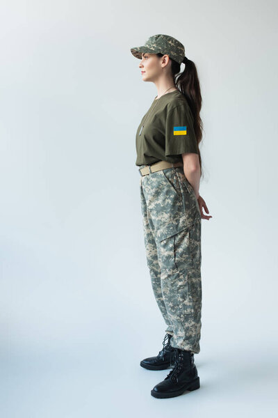 Side view of soldier with ukrainian flag on chevron looking away on grey background