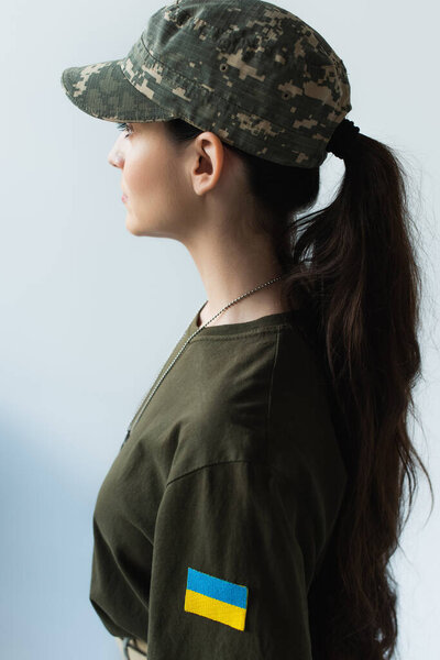 Side view of young soldier with ukrainian flag on chevron isolated on grey 